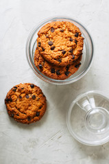 Stack of  homemade chocolate chip cookies in glass jar. White stone background.