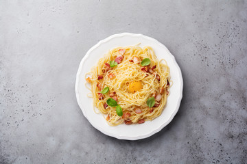 Pasta spaghetti carbonara with bacon, parmesan cheese, egg yolk and basil leaves on gray light background. Traditional Italian dish. Top view.