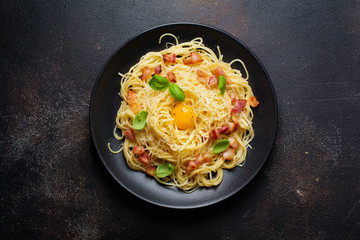 Pasta spaghetti carbonara with bacon, parmesan cheese, egg yolk and basil leaves on black background. Traditional Italian dish. Top view.
