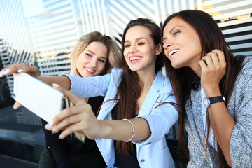 Three women taking a selfie while shopping in a clothing store. They are happy and smiling at camera. Shopping concept, also related to social media addiction.