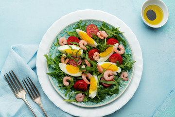 Arugula, cucumber, tomato, eggs and shrimp salad with soy sauce on ceramic plate. Selective focus. Top view.