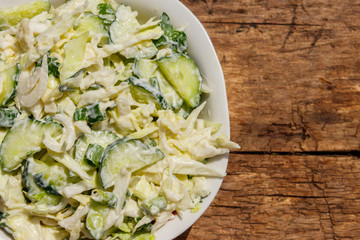 Spring salad with cabbage, cucumber, green onion, parsley and mayonnaise on wooden table