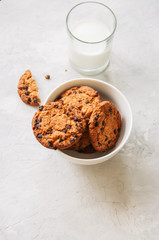 Homemade chocolate chip cookies in a bowl and glass of fresh milk on a white stone background.