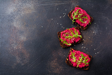 Bruschetta with beetroot hummus, arugula and sesame seeds on dark concrete background. Top view.