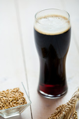 glass of dark beer with wheat on a wooden table background