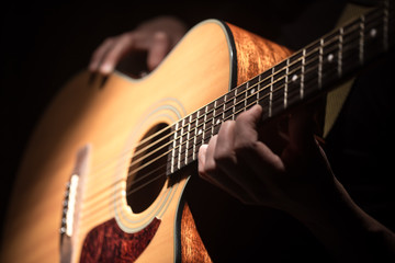 Obraz premium Man playing acoustic guitar on dark background. A musical concept.