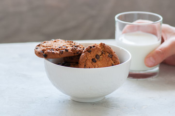 Homemade chocolate chip cookies in a bowl and glass of fresh milk on a white stone background.