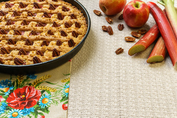 Whole apple and rhubarb pie with pecan on a black tray on a table.