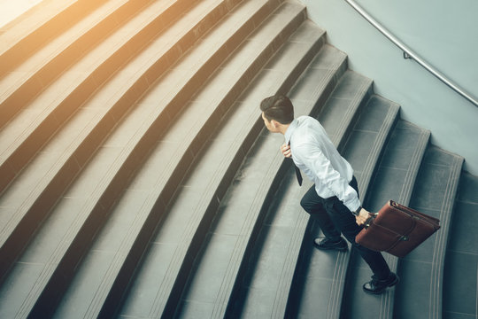 Businessman holding suitcase and running on stairs.