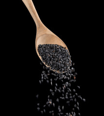 Black sesame falling from wood spoon on black background