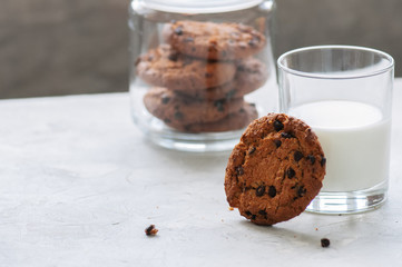 Homemade chocolate chip cookies and glass of fresh milk on a white stone background.
