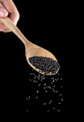 Black sesame falling from wood spoon on black background