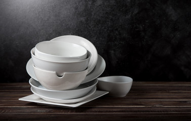 Stack of white ceramic dishware on wood against black cement wall
