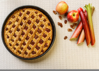 Whole apple and rhubarb pie with pecan on a black tray on a table.