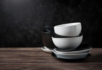 Stack of white and black ceramic dishware on wood against black cement wall