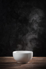 Steam of hot soup with smoke in ceramic bowl against black cement wall