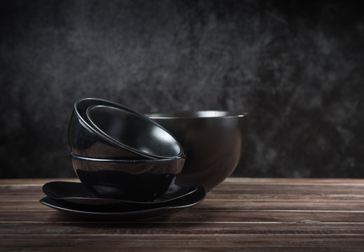 Stack of black ceramic dishware on wood against black cement wall
