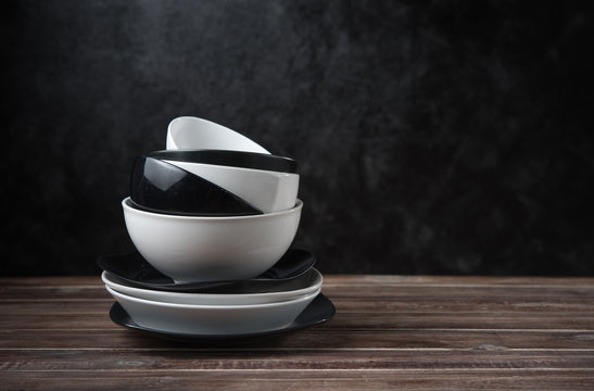 Stack of white and black ceramic dishware on wood against black cement wall