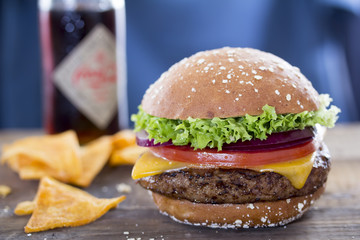 Burger with lettuce, tomato, onion and cheese & tortilla chips and drink