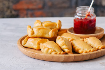 Two types of empanadas on a wooden plate with ketchup. White stone background.