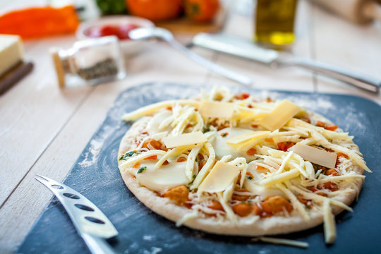 closeup raw fresh homemade traditional italian cheese pizza ready to cook on wooden cooking table with ingredients. wallpaper for pizzeria and food concept