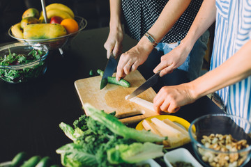 Two women cutting fresh vegetables for green veggie salad, healthy food cooking