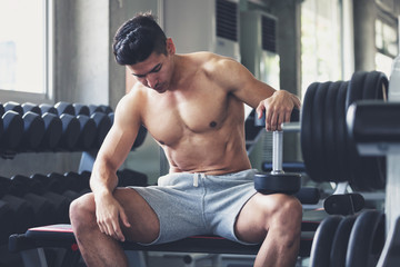 Fitness man with dumbbell tired and resting in gym