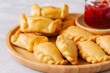 Two types of empanadas on a wooden plate with ketchup. White stone background.