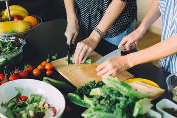 Two women cutting fresh vegetables for green veggie salad, healthy food cooking