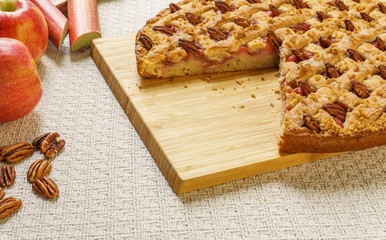 Cutted apple and rhubarb pie with pecan on a black tray on a table.