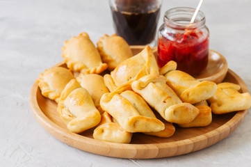 Two types of empanadas on a wooden plate with ketchup. White stone background.
