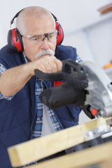 senior carpenter cutting wooden plank with circular saw