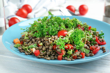 Plate with delicious lentils salad on wooden table