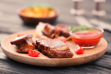 Wooden plate with delicious grilled ribs on table