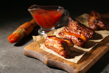 Wooden board with delicious grilled ribs on table