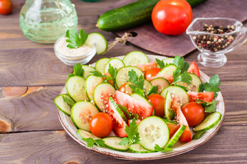 Vegetable salad of fresh cucumbers, tomatoes, parsley and sesame seeds on a plate on a wooden table