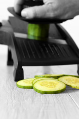 Man slicing cucumber with a mandoline on a grey wood kitchen worktop with selective colour