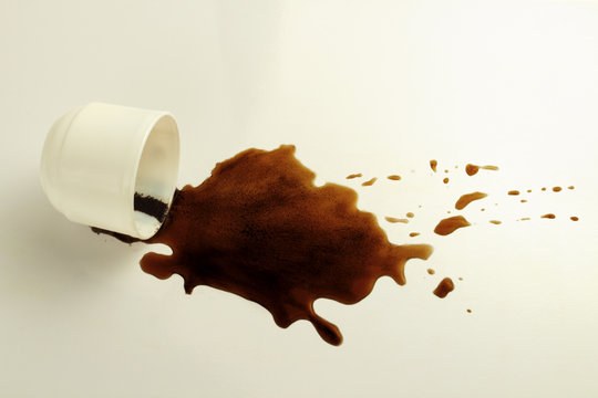 White cup and spilled black coffee on a white background