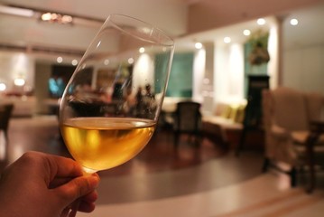 A hand holding wineglass in dinner, selective focus with blurred interior of restaurant background. Low key.