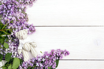 Lilac flowers with toy bear on white wooden background. Copy space.