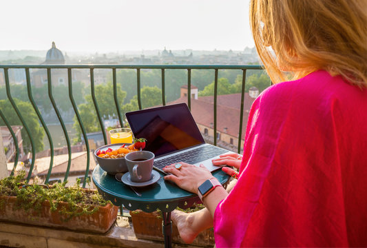 Woman using laptop during breakfast on balcony