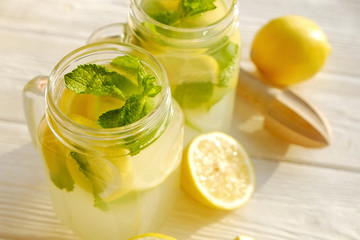 Two mason jar glasses of homemade refreshing lemonade, slices of organic ripe lemon, whole and halved, mint leaves, juicer, muddler, squeezer on a rustic white wooden background. Close up, top view.