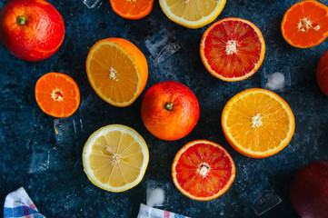 Mix of fresh ripe citrus fruits as blood oranges, mandarines, lemons  with ice cubes on a blue stone background. Top view.