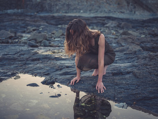Young woman by rock pool on coast at sunset