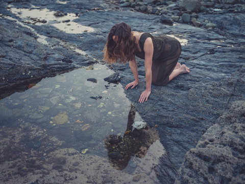 Young woman by rock pool on coast at sunset