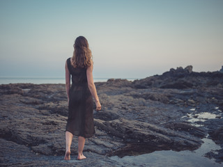 Young woman walking on coast at sunset
