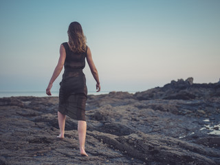 Young woman walking on coast at sunset