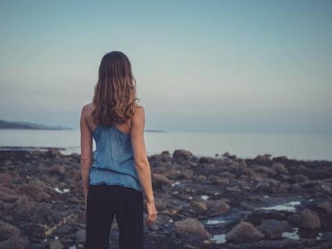 Young woman standing on coast at sunset