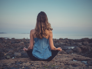 Fototapeta na wymiar Young woman meditating on coast at sunset