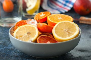 Mix of fresh ripe citrus fruits as blood oranges, mandarines, lemons  with ice cubes in a bowl on a blue stone background.